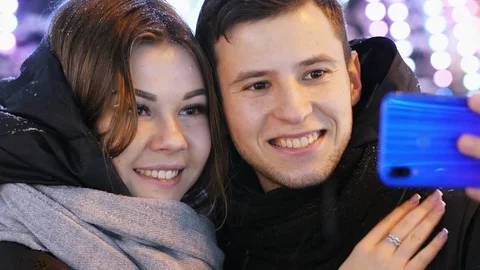 Close-up of happy couple makes a selfie on a modern phone, smiling and kissing Stock Footage 100644487