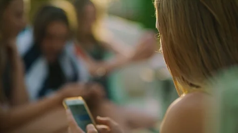 Close up of happy girls sitting poolside using social media on cell phones / Stock Footage