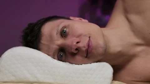 Close-up of a happy man waking up on a memory foam pillow, smiling and looking Video stock 297864244