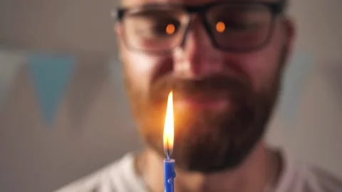 Close-up Happy smiling young bearded man blows out a candle on a birthday cake Stock Footage 202201570