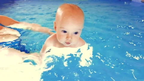 Close-up of a happy toddler learning to swim and swimming with an instructor in Stock Footage 240311282