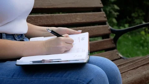 Close up of happy woman taking notes into notebook using pencil at a park Video stock 100628759
