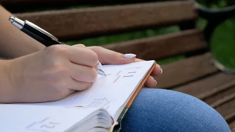 Close up of happy woman taking notes into notebook using pencil at a park Video stock 100628776