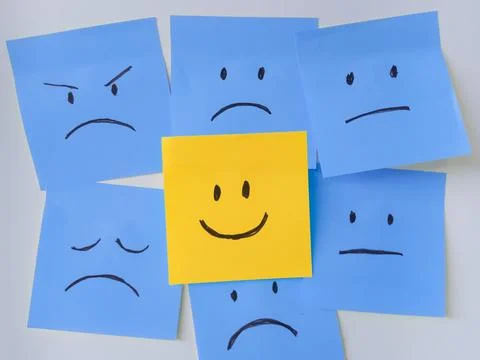 Close Up of Happy Yellow Sticky Note Among Sad Blue Notes on White Background Stock Photos
