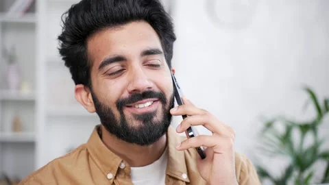 Close up. Happy young handsome man talking on smartphone while sitting in living Stock Footage 252205402