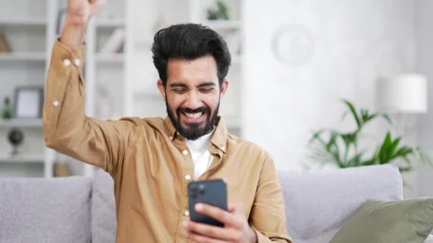 Close up Happy young man received great news on smartphone while sitting on sofa Stock Footage 252201490