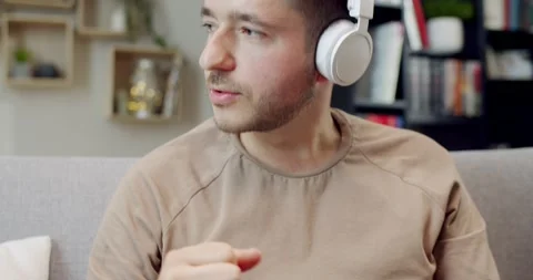 Close up of happy young man sitting in cozy room on couch and listening to music Stock Footage 220372076