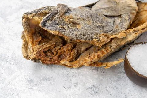 Close-up of the head of a salted cod next to a bowl with grains of sea salt Stock Photos