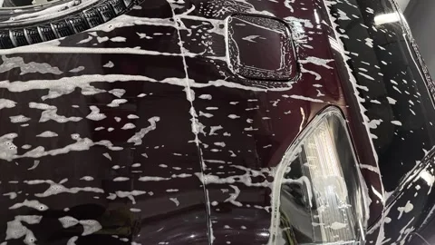 Close up of headlight, wheel, side of an eggplant-colored car covered with foam Stock Footage 243628612