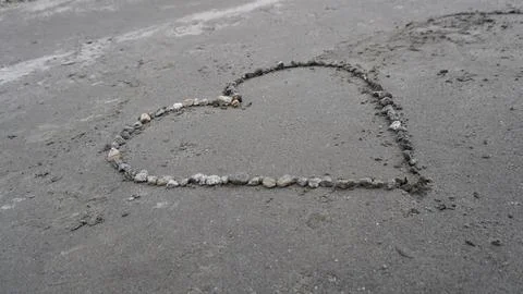 Close-up of a heart shape drawn in small pebbles on gray concrete, detail. Stock Photos