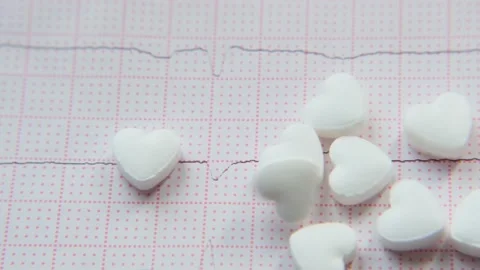 Close-up heart-shaped tablets falling on ECG. Medical video background. Stock Footage 202790691