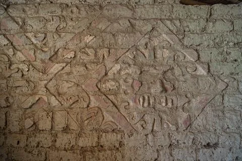 Close up of a heavily eroded adobe relief featuring the faded stylized face of t Stock Photos