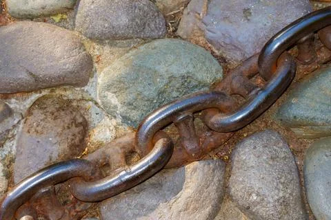 Close-up of heavy rusty chain lying across rounded cobblestone pavement in .. Stock Photos