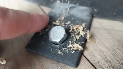 Close-up of a hexagonal metallic bolt screwed into a black metal bracket with wo Stock Footage 335474889