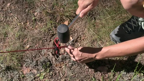Close up high angle shot of person hammering tent peg with rubber mallet in Stock Footage 339094124
