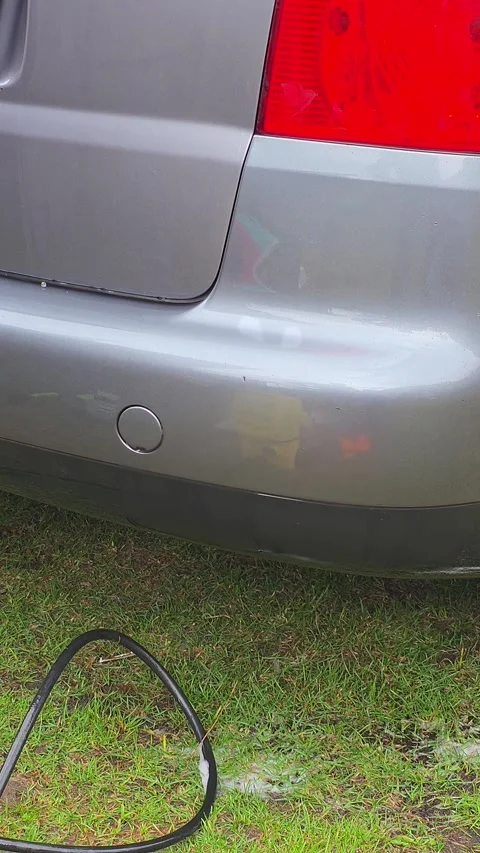 Close-up of high-pressure water spray washing a grey car rear bumper on gre.. Vídeo Stock 331959765