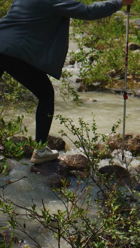 Close-up of hiker crossing mountain stream using trekking poles Stock Footage 335568734