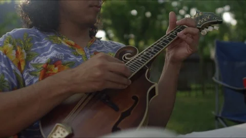Close-up of a hispanic man playing a mandolin in the backyard with a lens flare Video stock 125728330