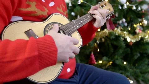 Close up of hispanic man playing ukulele in front of a Christmas tree. Video stock 140863992