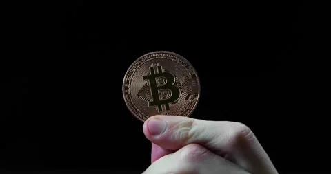 Close-up holding a copper Bitcoin coin in front of a black background Stock Footage 295026101