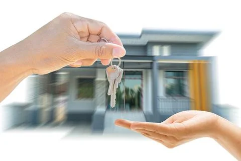 Close up holding house key giving other in hand. Blurry home background. Stock Photos