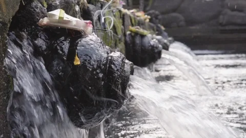 Close-up of holy spring water stream pouring into pool and traditional Balinese Stock Footage 86295606