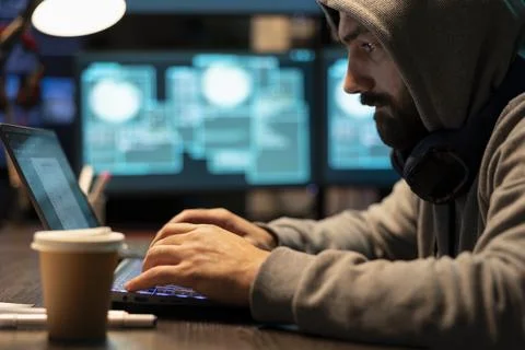 Close up of hooded man typing code on laptop in dark office 库存照片