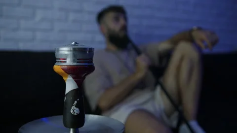Close-up of a hookah against which a man is sitting and exhaling smoke Stock Footage 204844144