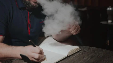 Close-up of hookah in men's hands. A man with a small beard exhales smoke in Stock Footage 253491981