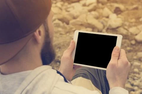 Close-up of a horde in a brown cap in the open air holds a white tablet pc in Stock Photos