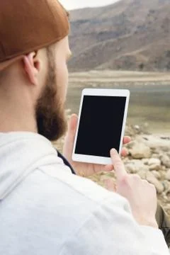 Close-up of a horde in a brown cap in the open air holds a white tablet pc in Stock Photos