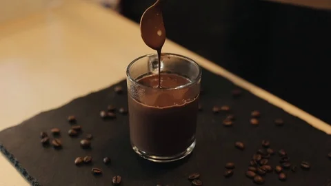 A close-up of hot chocolate falling from a spoon into a full glass mug Stockbeeldmateriaal 113950123