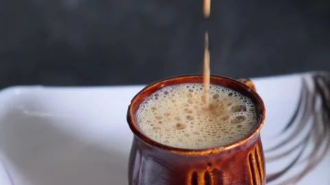 Close-up of hot frothy masala tea or chai being poured into a brown ceramic cup Видео 329975135