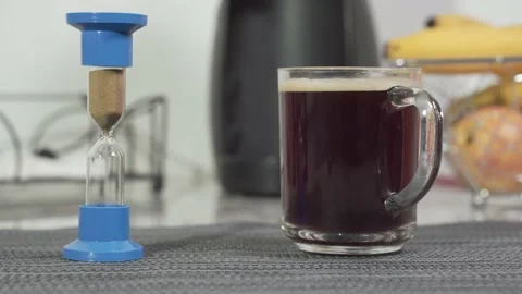 Close-up of hourglass with coffee cup on the table. Coffee time. Stock Footage 145992177