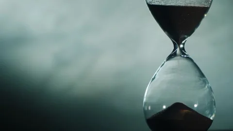 Close up of hourglass measuring passage of time with flowing sand against d.. Stock Footage 334657519