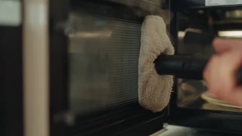 Close-up of housekeeper sanitizing microwave interior using steam cleaner and Stock Footage 311053930
