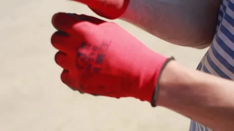 Close-up of how man in a striped T-shirt puts his hands on red rubberized gloves Stock Footage 247020909