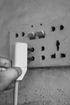 A close-up of a human hand inserting a two-pin electric plug into a wall so.. Stock Photos