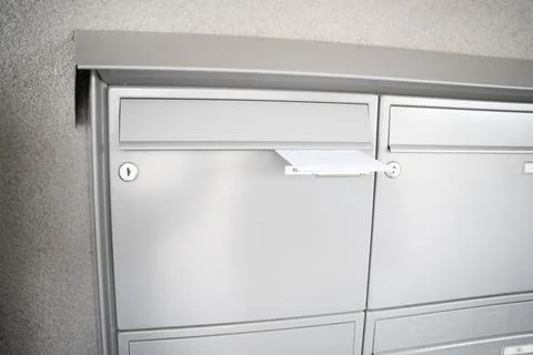 A close-up of a human hand inserting a white envelope in a row of grey metal mai Stock Photos