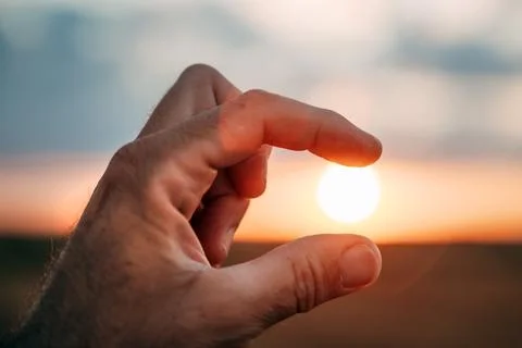 Close-up of a human hand pinching the setting sun between two fingers again.. Stock Photos