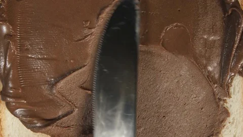 CLOSE UP: Human hand spreads a chocolate paste on a bread Stock Footage 70806732