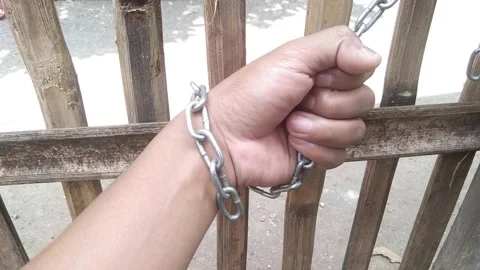 Close-up of human hand tied with iron metal chain against bamboo wooden fen.. Stock Footage 341536042
