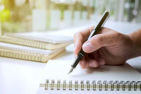 Close-up human hand writing something on paper notebook in sunlight backgroun Stock Photos