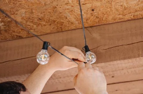 Close-up of human hands hanging a warm string of decorative light bulbs fro.. Stock Photos