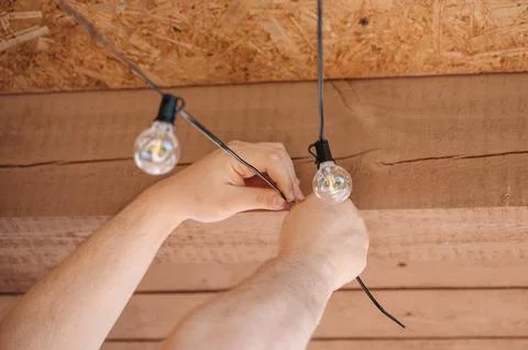 Close-up of human hands hanging a warm string of decorative light bulbs fro.. Stock Photos