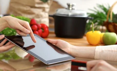 Close-up of human hands using tablet or touch pad. Two women in kitchen. Cooking 库存照片