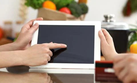 Close-up of human hands using tablet or touch pad. Two women in kitchen. Cooking Stockfoto's