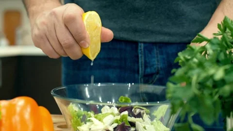 Close-up human Squeezes a Half Cut Lemon over a Salad in Kitchen. Cooking V.. Stock Footage 265840667