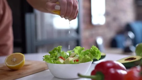 Close-up human Squeezes a Half Cut Lemon over a Salad in Kitchen. Cooking V.. Stock Footage 265840692