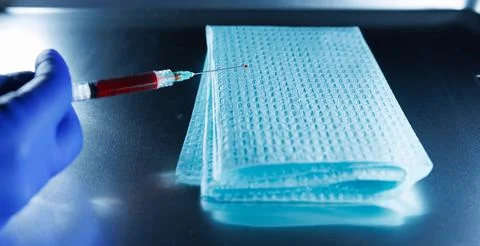 Close-up of a hypodermic needle with a drop of blood at the tip being held .. Stock Photos